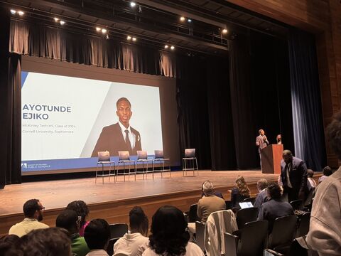 Ayotunde speaking at a DCPS leadership event, beside a screen introducing him